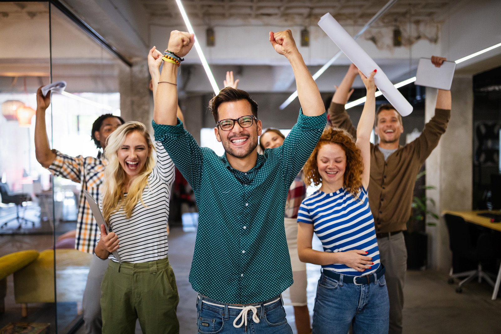 Grupo de pessoas em um escritório, sorrindo e com os braços levantados.